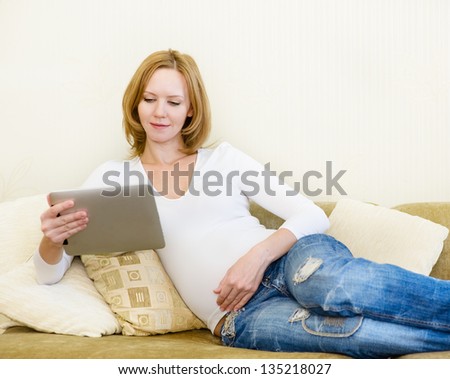 pregnant woman lying down on sofa and using electronic tablet