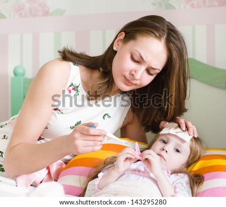 Sick kid with high fever laying in bed and mother taking temperature