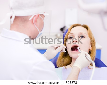 young woman with open mouth during drilling treatment at the dentist