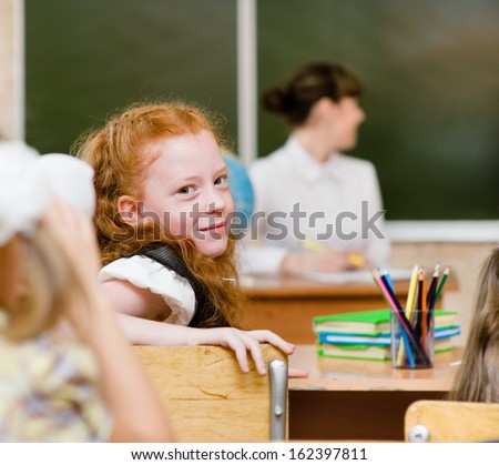 Portrait of schoolgirl at workplace with teacher on background