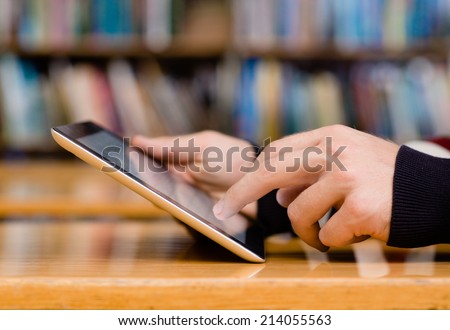 Hands typing on tablet computer in library