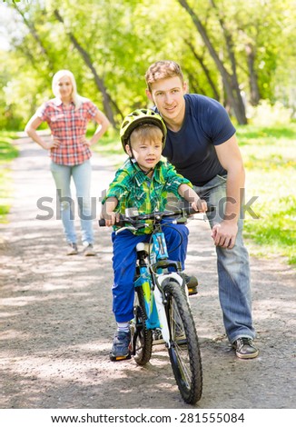 mother and  father teaches his son to ride a bike