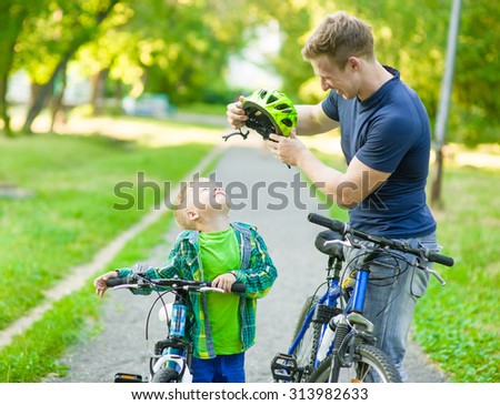young father trying to wear a bicycle helmet to his son