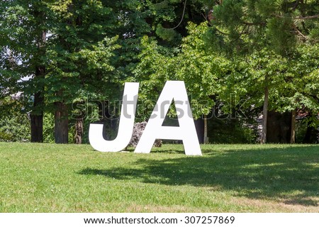 German Yes (Ja) written with upper case letters, on a green meadow with trees in the background