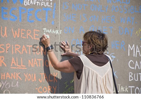 TORONTO, ON CANADA - 22 AUG:  Woman writing on the walk at the Jack Layton chalk memorial at Nathan Phillips Square on August 22, 2012 in Toronto, ON, Canada.