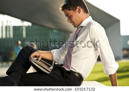 Relaxed businessman using his PC tablet while sitting on a bench