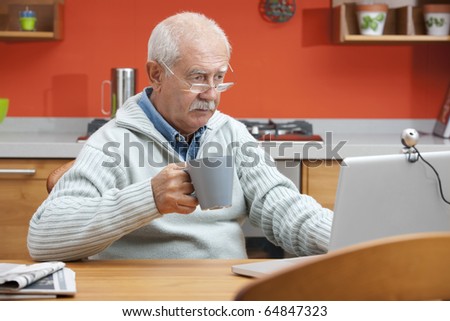 Senior man speaking through webcam in his kitchen