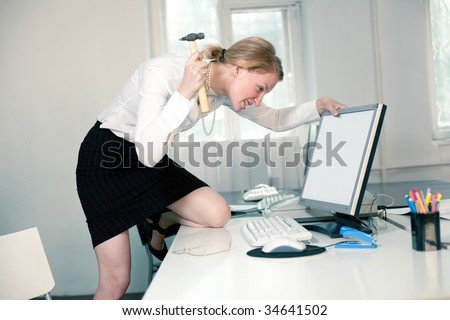Angry young woman stays by computer and hits it by hammer