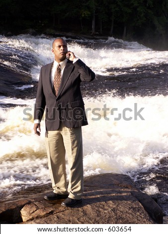 business man in a suit with cell phone standing on a rock in front of a river