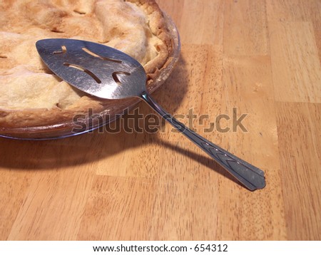 corner of a freshly baked apple pie ready to slice on a butcher block table. focus on spatula. shallow depth of field.