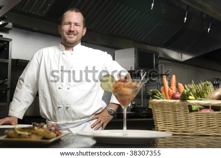 Attractive Caucasian chef standing in a restaurant kitchen with a basket of vegetables.