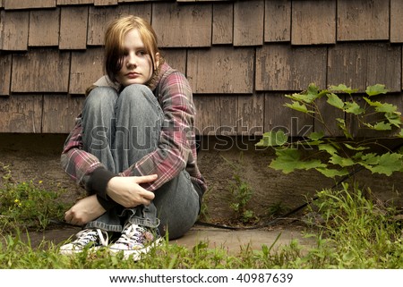 A Teenage Girl With A Sad Expression Sits Against A Run-Down House ...
