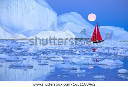 Sail boat with red sails cruising among ice bergs during dusk in front of a full moon. Disko Bay, Greenland.