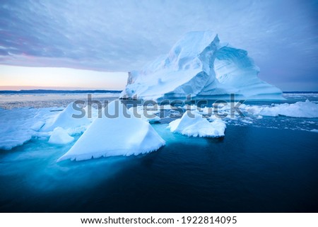 Photogenic and intricate iceberg with a hole under an interesting and colorful sky during sunrise. Disko bay, Greenland.