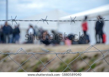 Barbed wire in refugee camp. Migrants behind chain link fence in camp. Group of people behind fence. Concept of prison, freedom, barrier, security and migration. Refugees on their way to EU. Stock foto © 
