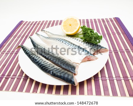 Raw mackerel fish filet on white plate, half a lemon and parsley on the side on purple wooden table cover