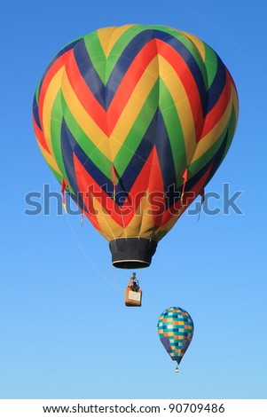 two hot air balloons float in a clear blue sky