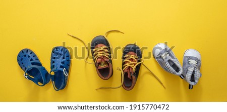 Baby first steps. Three pairs of boy blue shoes variety on yellow color background, top view. Kids footwear, beach sandals, booties and soft infant shoes in a row. Foto stock © 