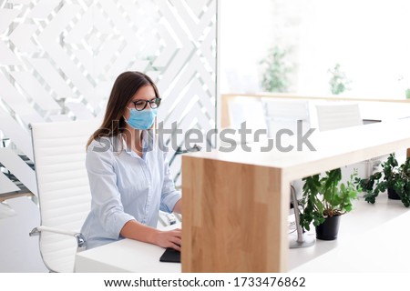 Receptionist wearing medical mask in office. Protection employees on workplace. Young woman working at reception in hotel. Disease prevention during quarantine, staff safety.