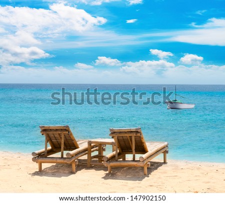 Tropical seascape with small boat bamboo beach beds under blue sky