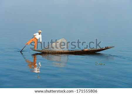 Traditional fisherman in wooden boat using a coop-like trap with net to catch fish in Inle lake, Myanmar