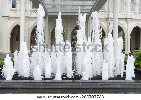 Several jets of water spurting skyward from an ornate fountain, in front of a beautiful and architecturally unique building in the background.