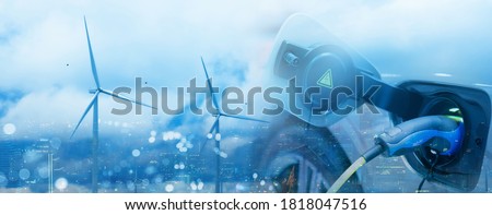 Double exposure of vehicle electric car charge battery with wind turbine and blue sky blur bokeh cityscape on panoramic background. Idea nature electric energy generate electricity. Green eco concept.