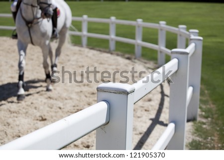 Riding a white horse. Horse riding track with sand on the ground, and a white horse in the background. Selective focus on the fence