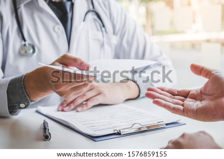 Doctor or physician writing diagnosis and giving a medical prescription to male Patient Imagine de stoc © 
