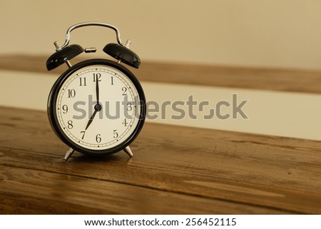 Vintage alarm clock on rustic wood table. Shows 7 o\'clock.