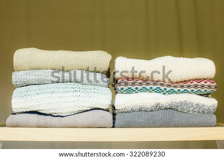 Two piles of warm sweaters for fall or winter on a shelf in a closet. Soft draped background.