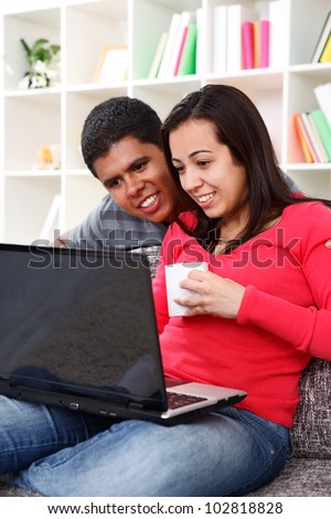 Happy couple browsing internet at home, using laptop computer, sitting on couch, smiling.