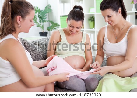 Three future mothers talking about baby clothes in living room