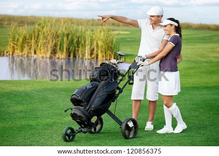 Golfers on golf course, smiling couple man pointing front of them
