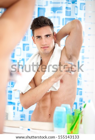 Young man applying roll-on deodorant front of mirror