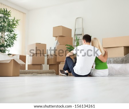 Young couple moving house resting in room full of boxes