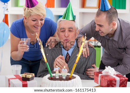 Senior man blowing candles with family and friends