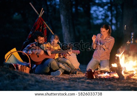 Family picnic in the woods with fire; Spring or autumn camping with campfire at night ; camping, travel, tourism, hike and people concept. Quality family time together.