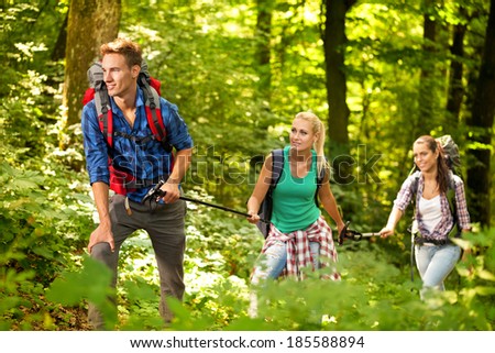 Three friends hiking through the forest, one male, two female, with backpacks
