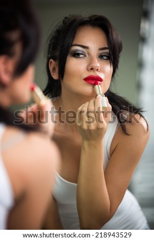 Woman doing make-up, beautiful young woman doing make-up and smiling while looking at the mirror