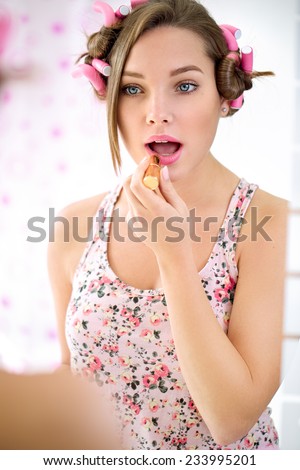 pretty young girl with curlers in front of the mirror putting lipstick