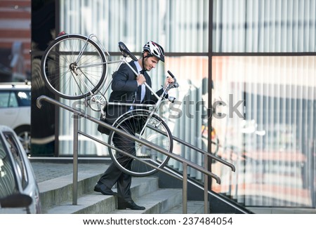 businessman with a cycle helmet on head carrying his bike down steps