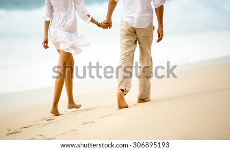 Back view of a couple taking a walk holding hands on the beach