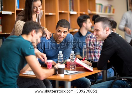 Few friends socializing and studying together for exam in library