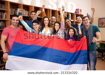 Happy group of students from Serbia with raised victory fists, presents their country with flag