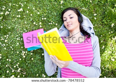 woman lying on grass with book and listening music on headset
