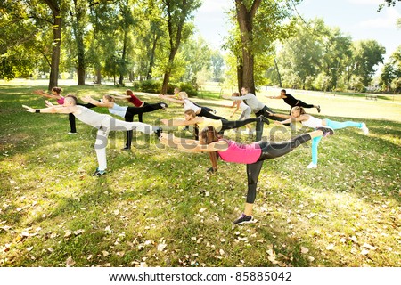 Group of young  people in park doing aerobics or warming up with gymnastics and stretching exercises