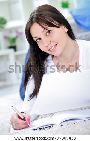 Happy teen girl learning on floor at home with books and pen in hand, smiling