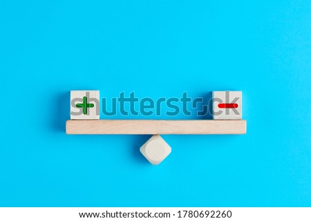 Plus and minus or positive and negative symbols on wooden blocks are in balance on a wooden seesaw. Blue background, flat lay view. Pros and cons equilibrium in decision making under uncertainity.  商業照片 © 