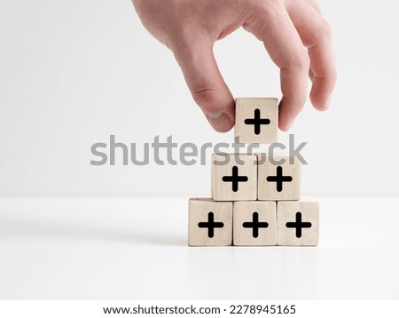 Added value or increasing benefits concept. Progress and profit to benefit growth and development in business. Hand places cube with plus symbol on top of the wooden cube pyramid. Сток-фото © 